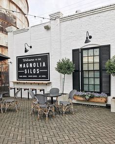 an outdoor dining area with tables, chairs and potted plants on the brick patio