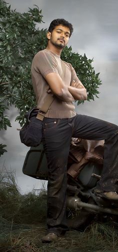 a man standing on top of an old car in front of a tree with his arms crossed