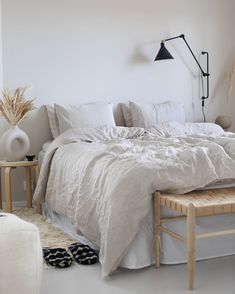 a bed with white linens and pillows in a bedroom next to a wall lamp