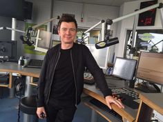 a man standing in front of a desk with computer monitors and microphones on it