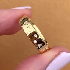 a gold ring with diamonds on it being held by someone's hand in front of a brown background