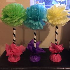 three different colored paper flowers in vases on a table with candy canes wrapped around them