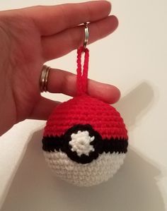 a crocheted poke ball ornament being held by a person's hand