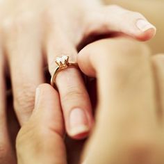 a close up of a person's hand holding a ring with a diamond on it