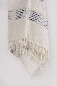 a white and blue towel hanging on the wall with tassels around it's edges