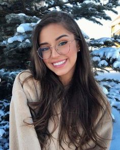 a woman wearing glasses standing in front of snow covered trees