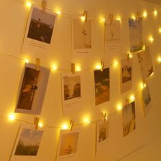 there are many pictures hanging on the wall with lights strung around it and some photos hung up