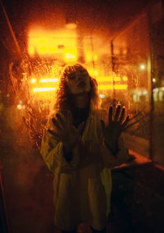 a woman standing in front of a window covered in rain