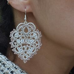 a close up of a woman's ear wearing white beaded earrings with filigrees