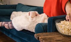 a woman laying on a couch with a bowl of popcorn in front of her