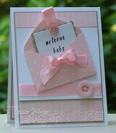 a welcome baby card with a pink bow and button on the front, sitting on top of a table