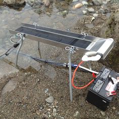 the solar panel is hooked up to an electrical device on the ground next to some rocks and water