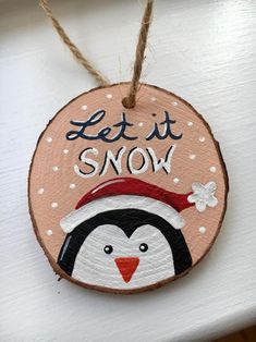 a wooden ornament that says let it snow with a penguin wearing a santa hat