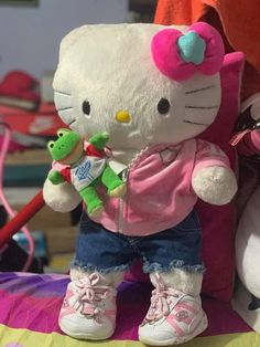 a hello kitty stuffed animal holding a frog on top of a bed next to another stuffed animal