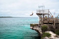 a person jumping off the edge of a cliff into the ocean from a pier on an island