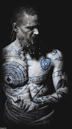 a man with many tattoos on his chest and arms, looking down at the camera