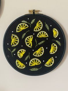 a black and yellow embroidered wall hanging on a white wall next to a plant with leaves