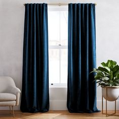 a living room with a chair, potted plant and blue curtains on the windowsill