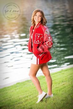 a beautiful young woman standing in front of a body of water wearing a red jacket