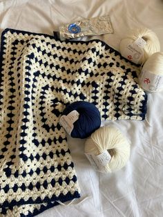 a crocheted blanket and balls of yarn on top of a white bed sheet