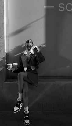 black and white photograph of a woman sitting on a wall with coffee in her hand