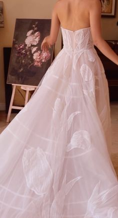 a woman in a white wedding dress standing next to a painting