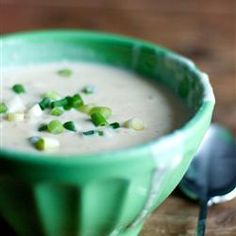 a green bowl filled with soup on top of a wooden table next to a spoon