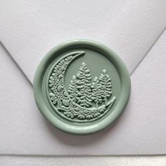 a green wax stamp with a tree and moon on it's side in an envelope