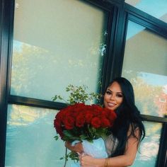 a woman holding a bouquet of roses in front of a large window with glass panes