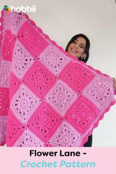 a woman holding up a pink crocheted blanket