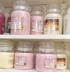 candles are lined up on shelves in a store, some with pink and white designs