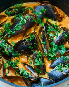 a pan filled with mussels covered in sauce and parsley