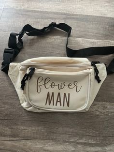 a white fanny bag with the words flower man on it sitting on top of a wooden floor