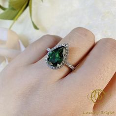 a close up of a person's hand wearing a ring with a green stone