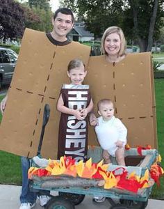 two adults and a child standing in front of a cardboard box with fire on it