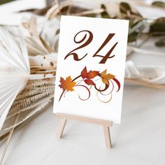 an easel with a table number decorated with autumn leaves