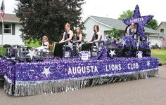 some people are riding on a float in the street with purple and silver decorations around them