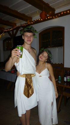 a man and woman dressed up in roman garb posing for the camera with beer cans