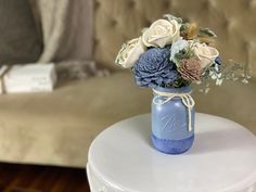 a blue mason jar filled with flowers sitting on top of a white table next to a couch