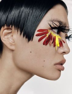 a woman's face with flowers painted on her cheek and eyeliners in the shape of feathers