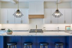 a kitchen with white cabinets and blue counter tops, three stools in front of the island