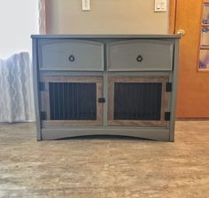 a grey cabinet with two doors and some drawers on the bottom, in front of a door