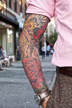 a man with a dragon tattoo on his arm is walking down the street in front of people