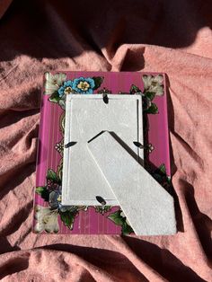 a pink and white square with flowers on it sitting on a bed next to a pair of scissors