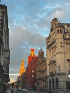 a city street filled with tall buildings under a cloudy blue and white cloud covered sky