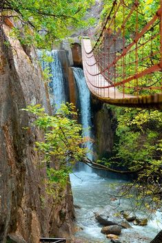 a suspension bridge over a river with a waterfall in the background