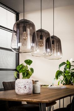 a wooden table topped with two vases filled with plants and hanging lights above it