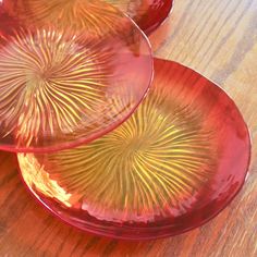 two red glass plates sitting on top of a wooden table next to each other,