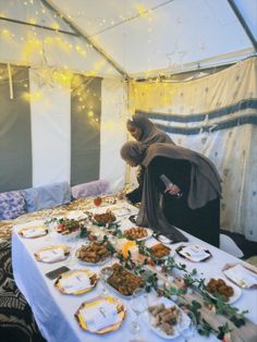 a woman in a hijab standing over a table covered with plates and food