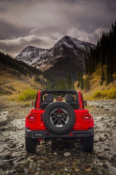 a red jeep parked on top of a rocky river